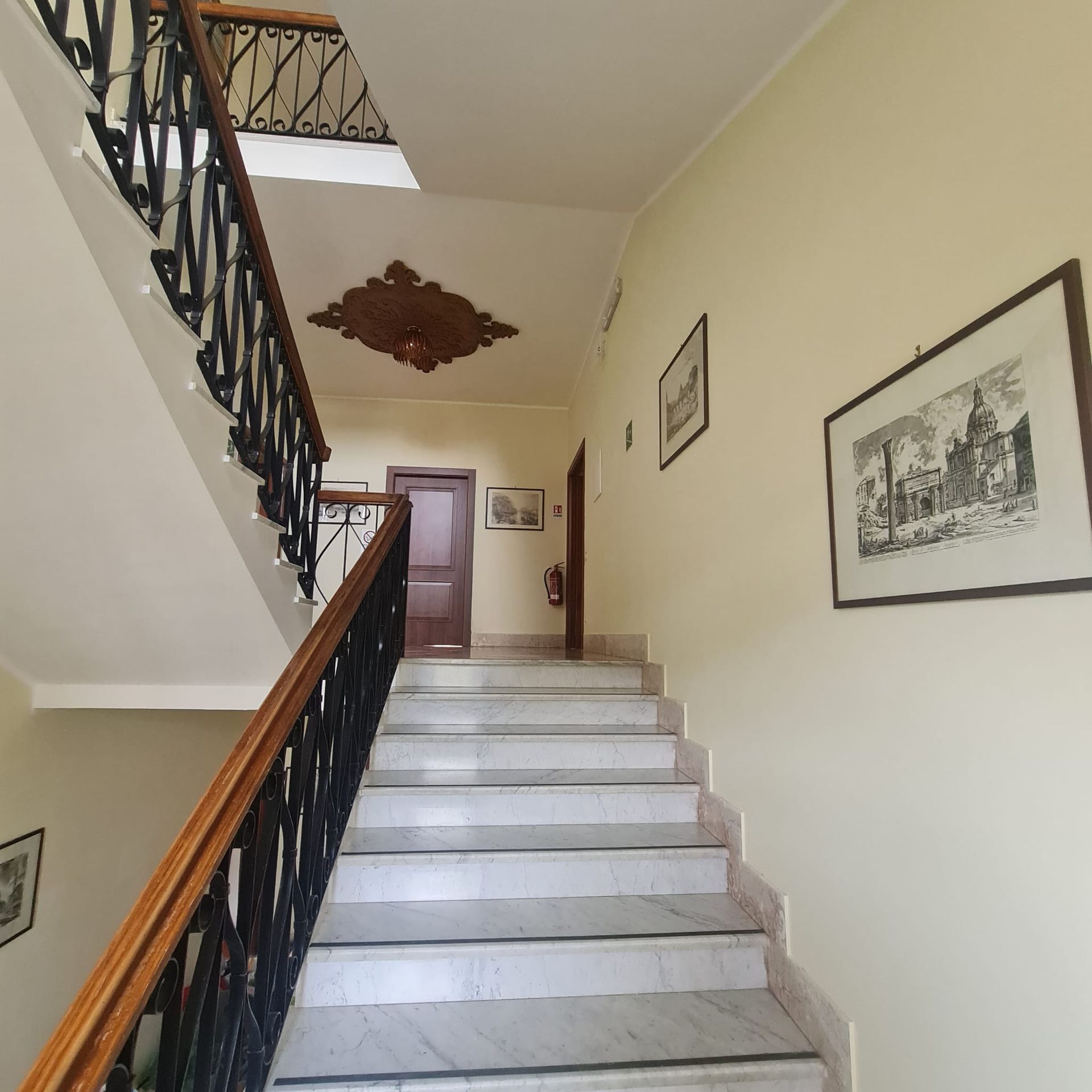 Scala interna con gradini in marmo bianco, ringhiera nera e quadro incorniciato in un corridoio.