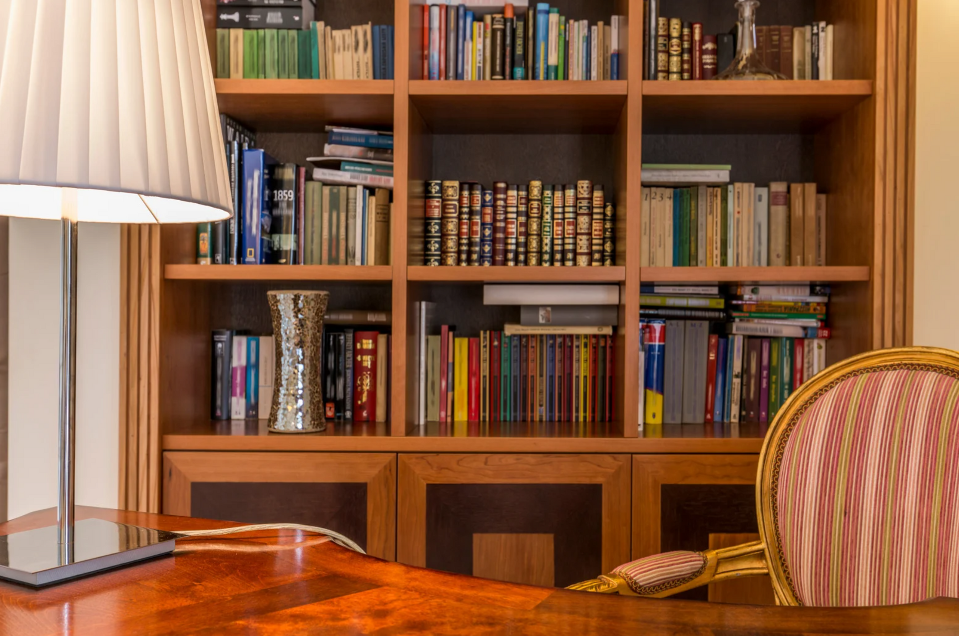 A desk with a lamp and a chair in front of a bookshelf filled with books.