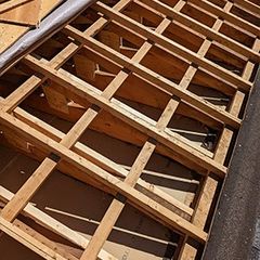 Structure de toiture en bois avec poutres apparentes, sous-couche visible.