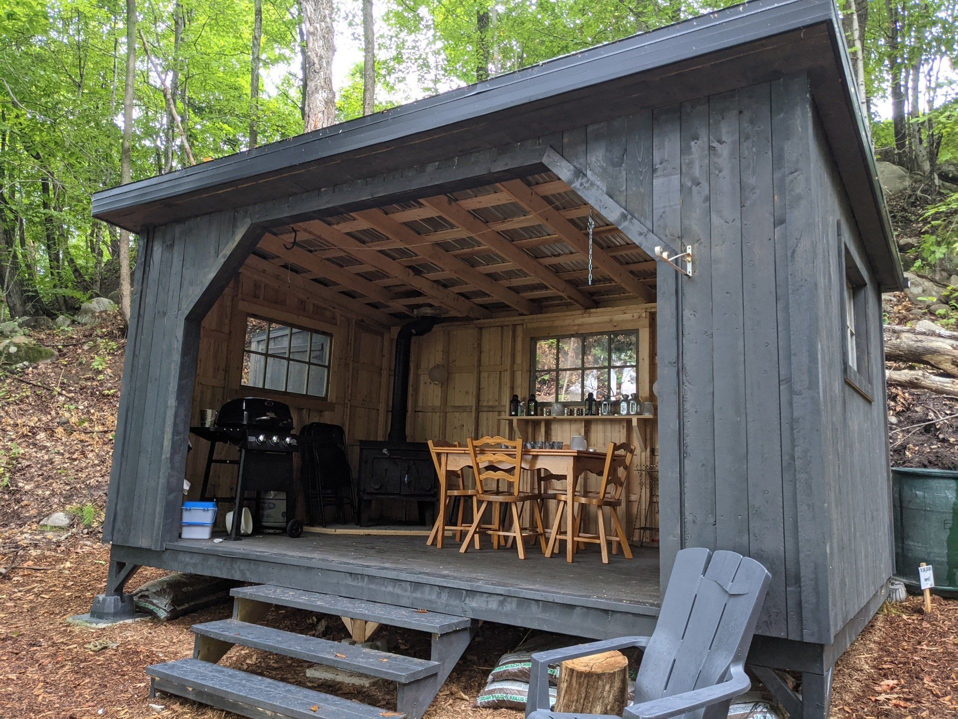 Cabane rustique avec un porche, un extérieur gris foncé, des marches en bois et des sièges extérieurs.