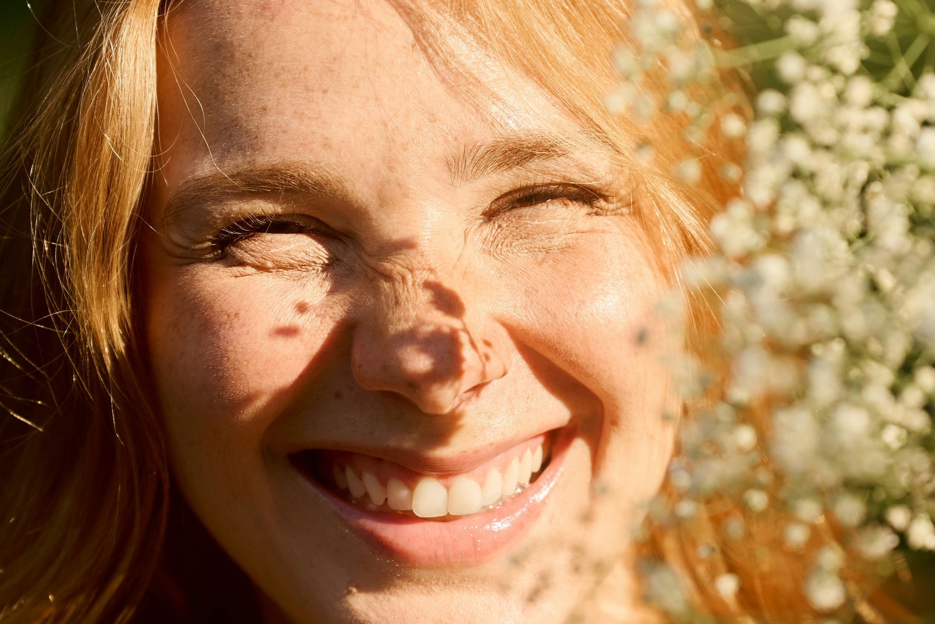 Joyful woman smiling in sunlight surrounded by flowers, capturing the confidence and lightness that can come from working with a top therapist in the Bay Area.