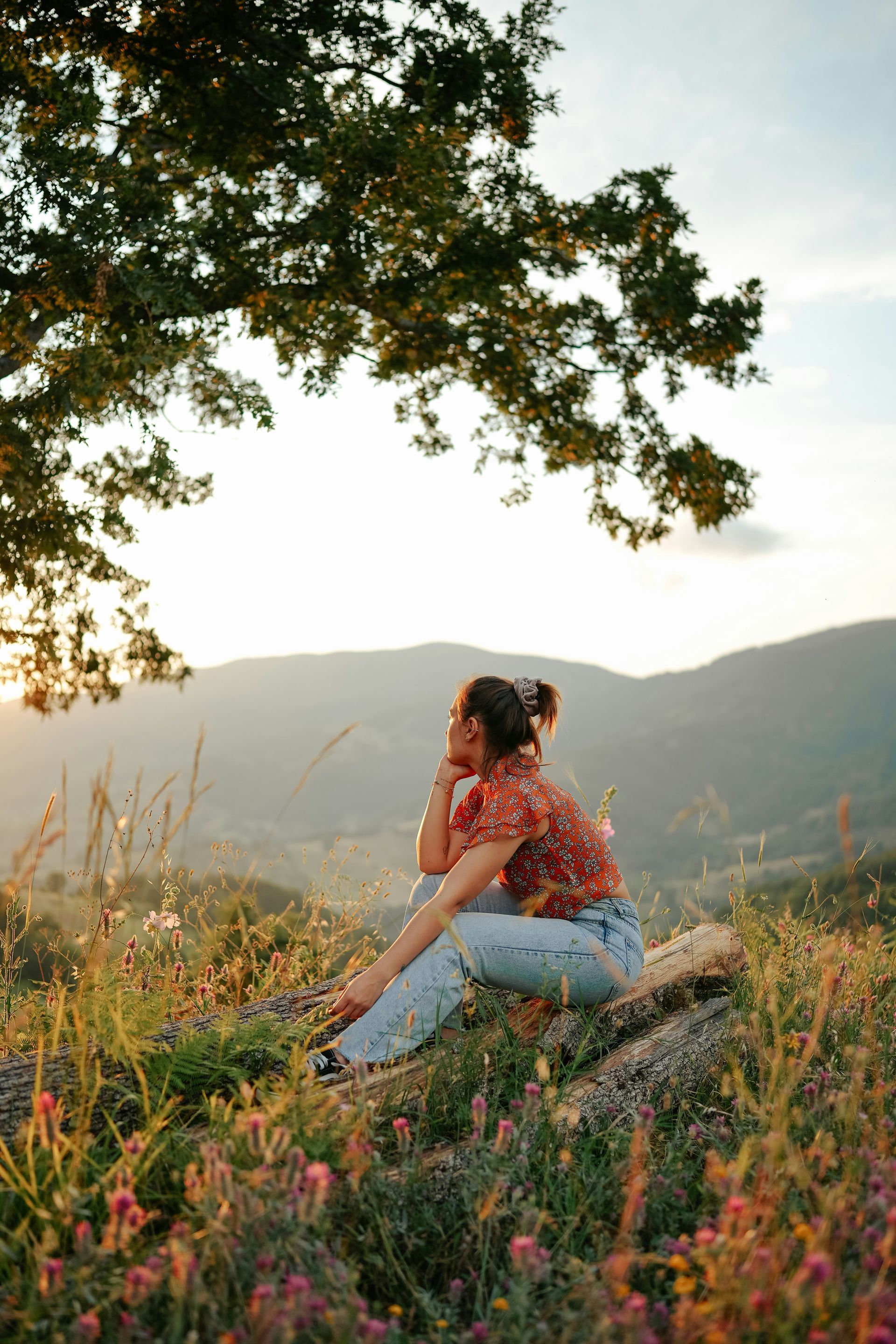 Woman sitting in nature at golden hour, representing the peaceful self-reflection that individual therapy with a Oakland therapist for women can offer.