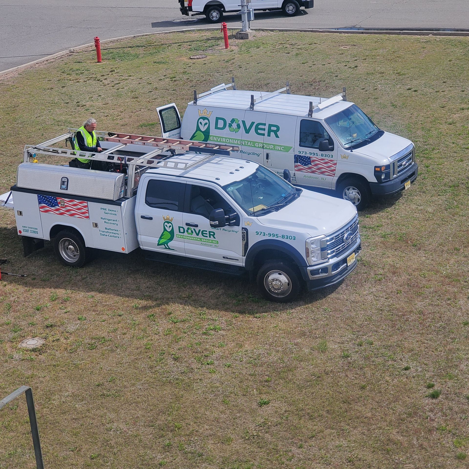 Two white utility trucks parked on grass, one marked Dover, with workers in safety vests nearby.
