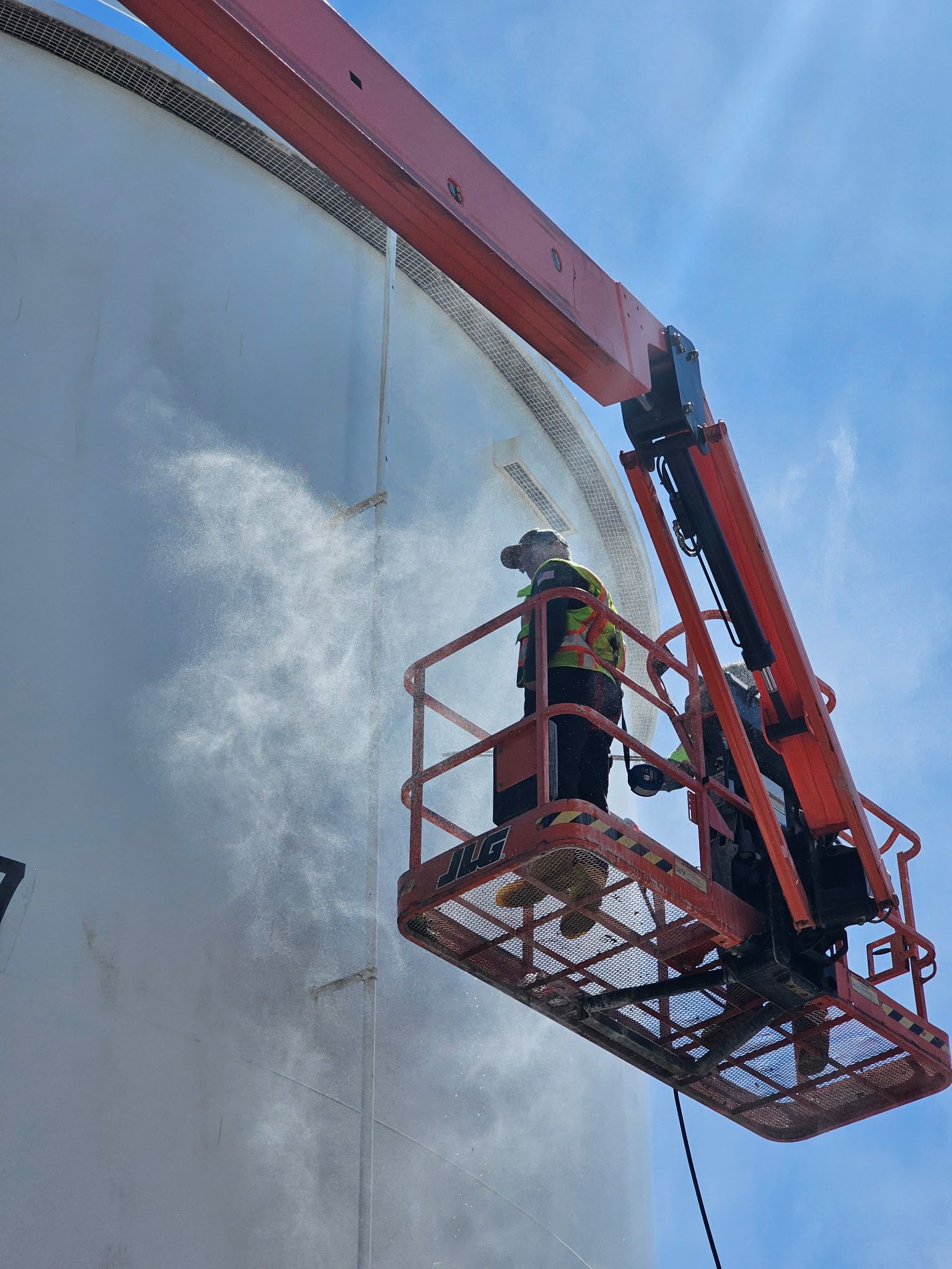 Worker in a red cherry picker spraying white paint on a large curved wall