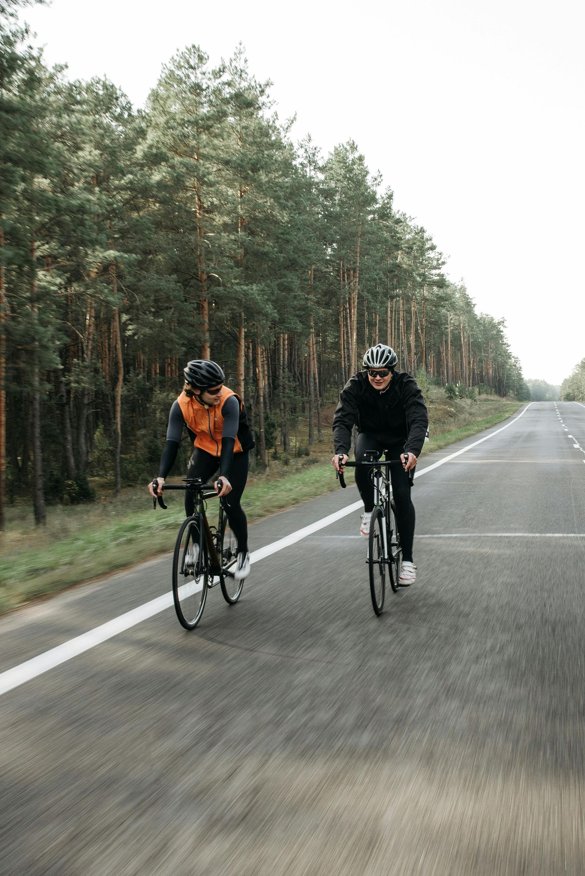 Two cyclists riding on a wet road beside a pine forest