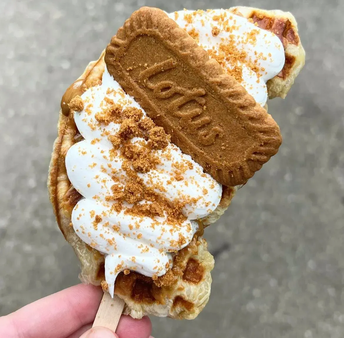 Soft serve ice cream in a cone, topped with a Biscoff cookie and cookie crumbs, held in hand