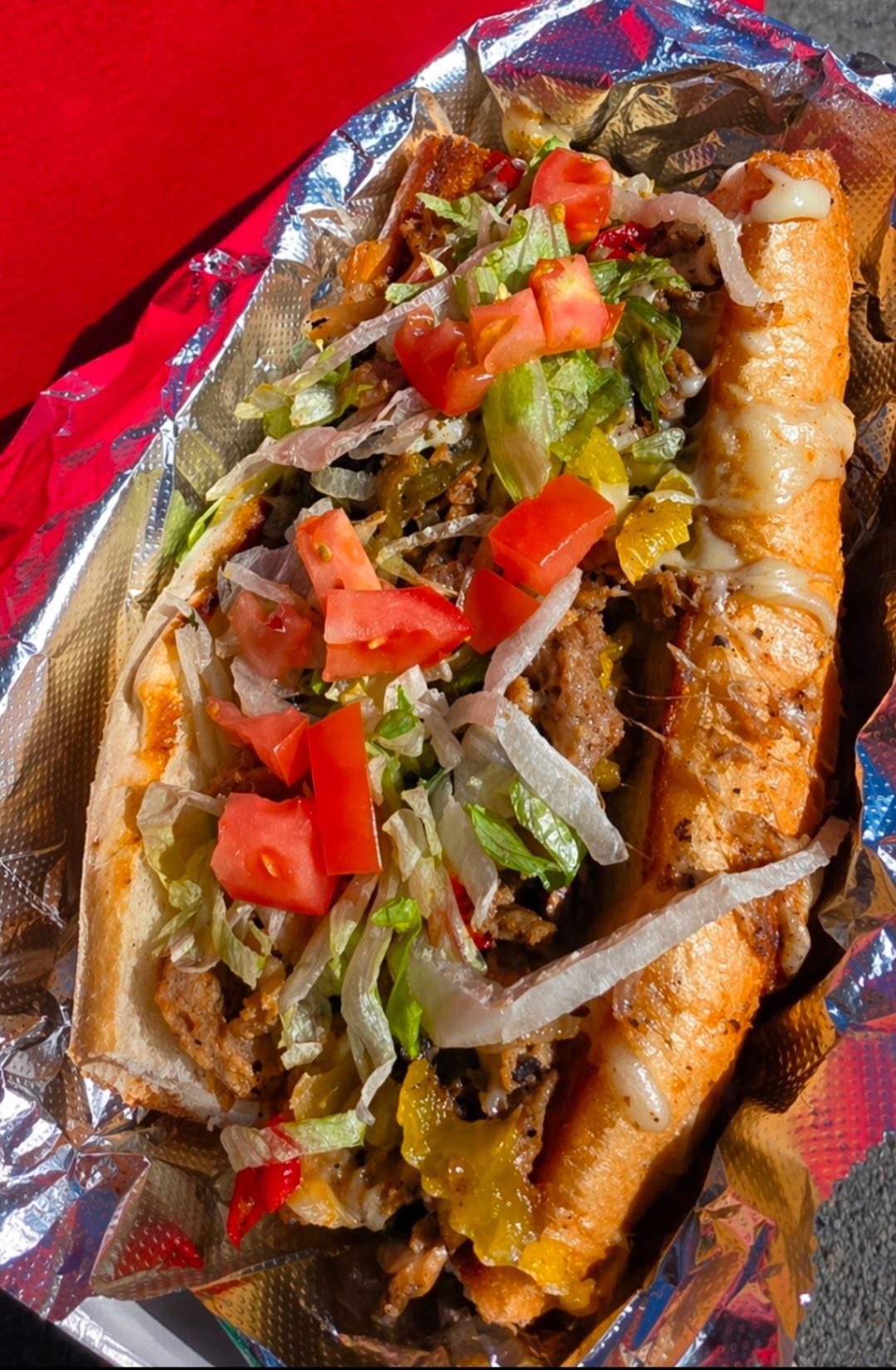 Grilled sandwich with melted cheese, tomato, lettuce, and peppers on foil