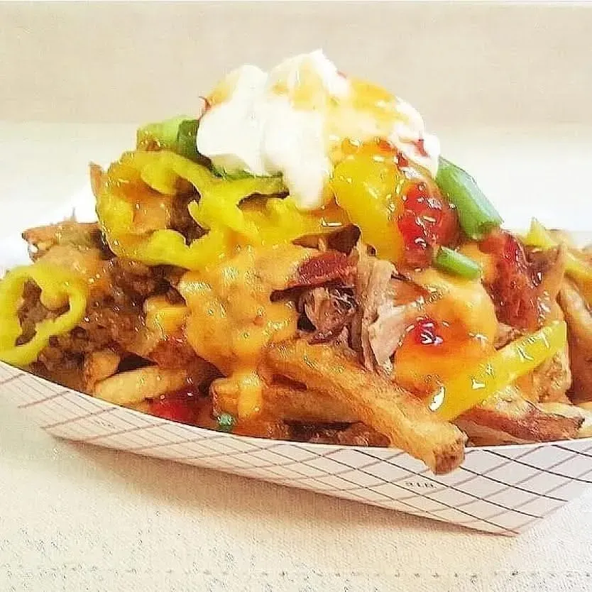 Loaded fries topped with melted cheese, sour cream, green peppers, and sauce in a paper tray