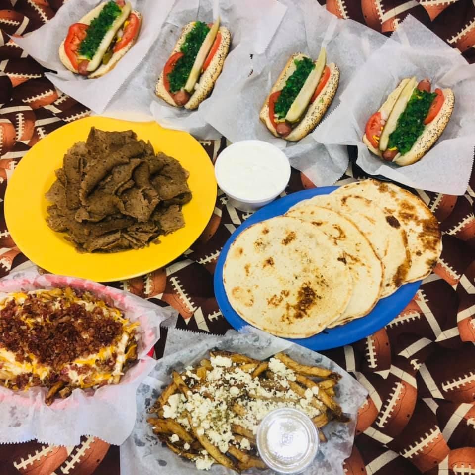 Assorted homemade dishes on a patterned cloth, including flatbreads, rice, meat, and stuffed sandwiches.