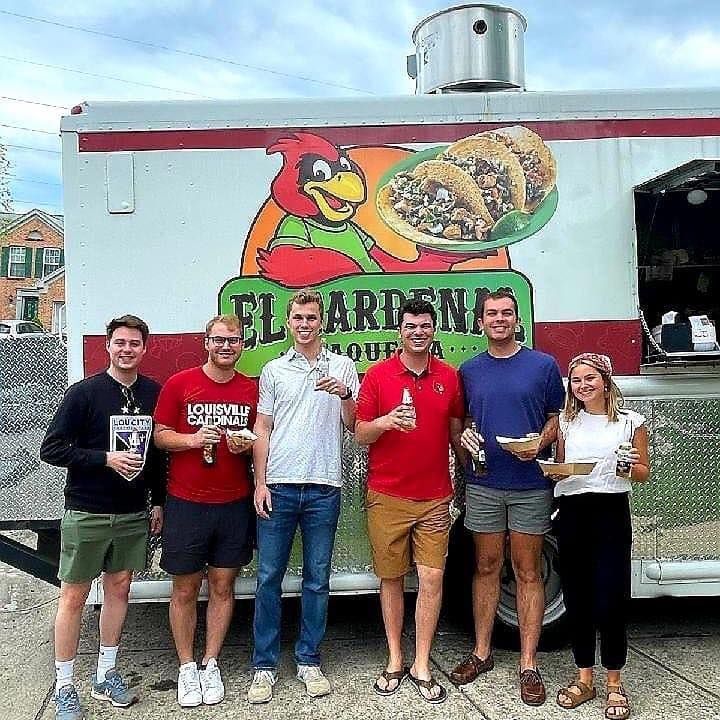 Six people posing in front of a colorful food truck mural, holding drinks and smiling.