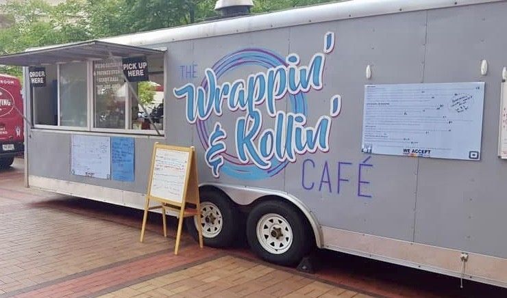 Gray food trailer with colorful “Wrappin’ & Rollin’ Cafe” sign parked outdoors