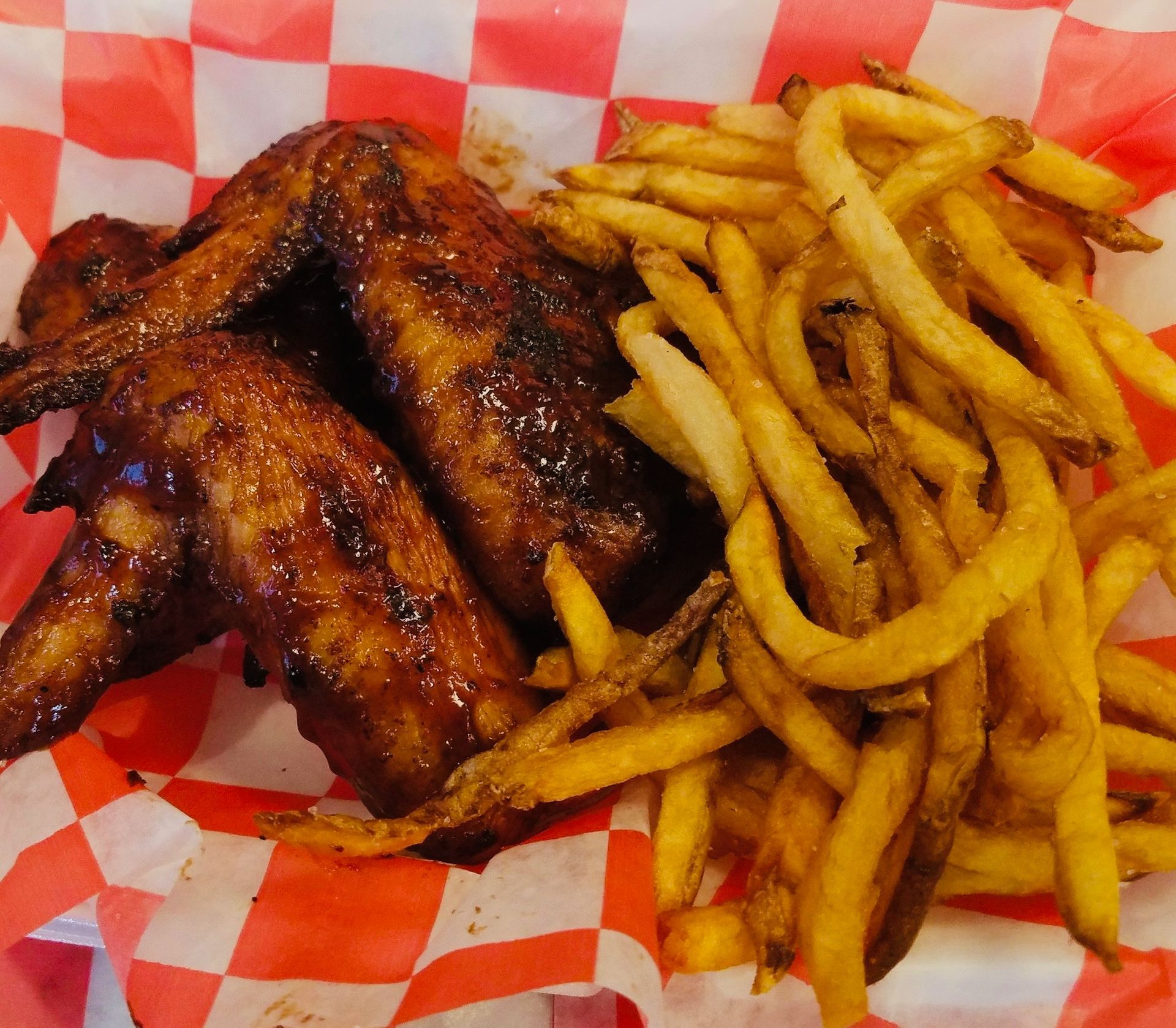 Grilled chicken wings and French fries on red-and-white checkered paper inside a takeout basket