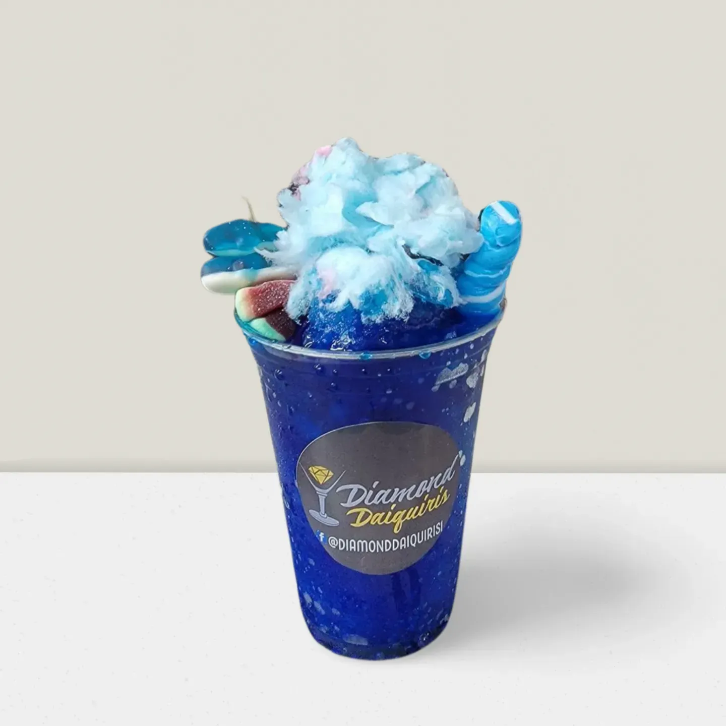 Blue dessert drink topped with cotton candy and candy pieces in a clear blue cup