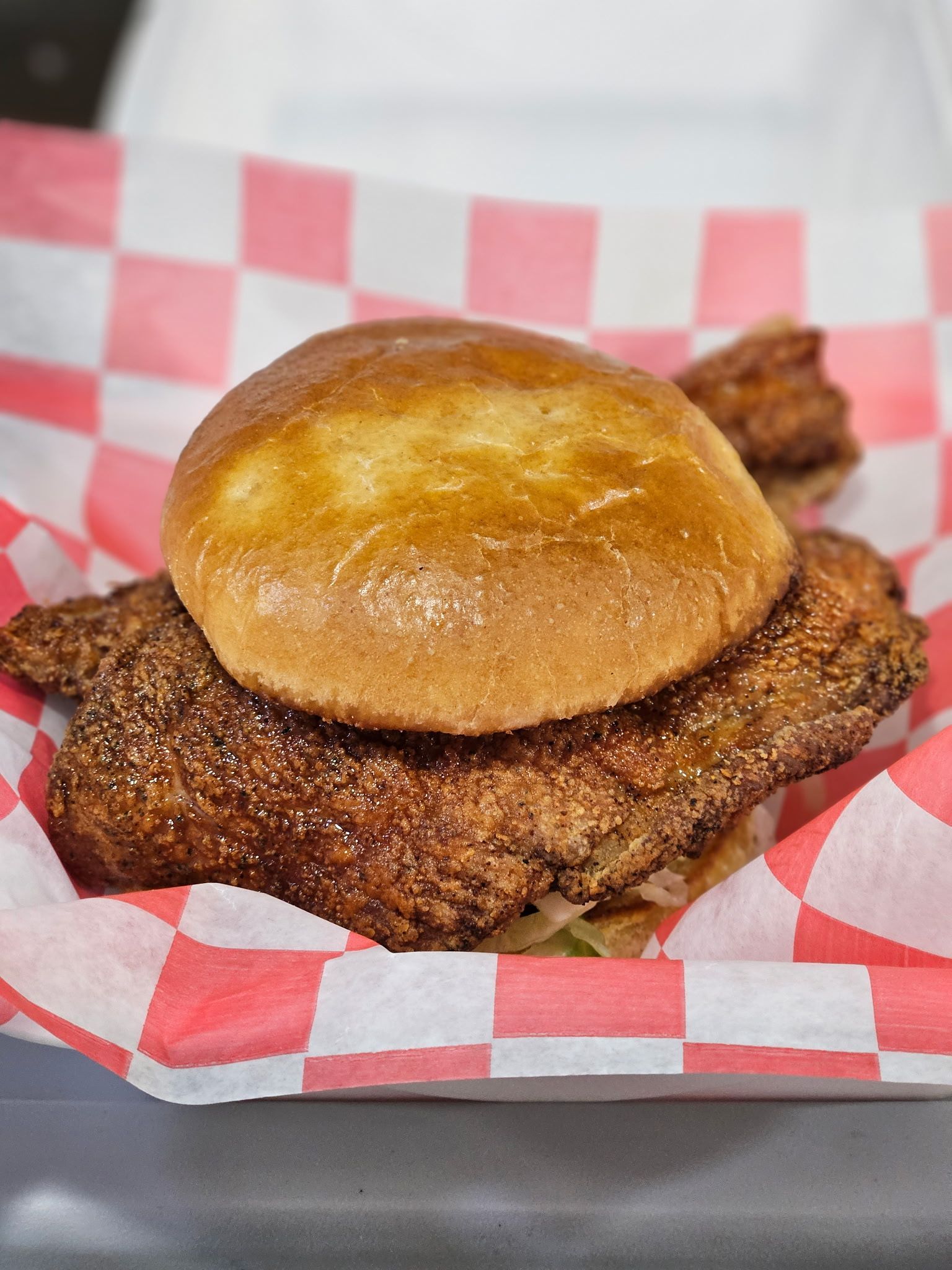 Fried chicken sandwich on a bun in red-and-white checkered paper basket liner