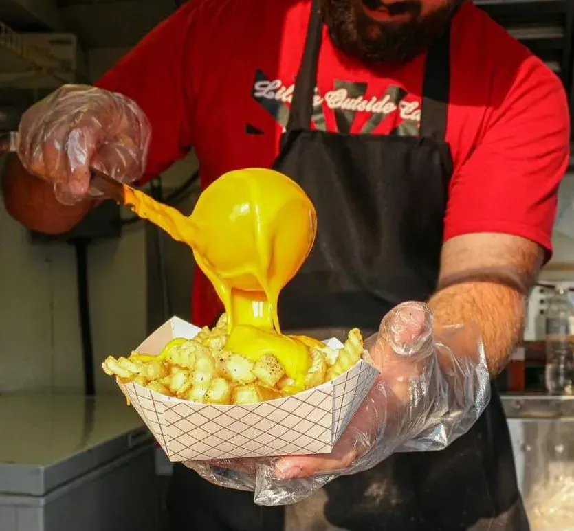 Vendor pouring bright yellow sauce over fries in a paper tray at a food stall