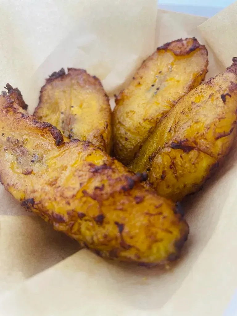 Three golden-brown fried plantains in a paper-lined container