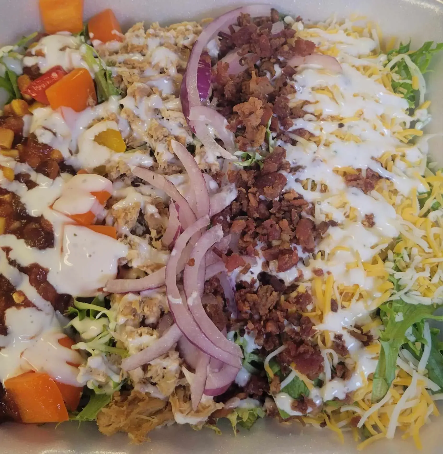 Burrito bowl with rice, shredded cheese, lettuce, onions, beef, and diced vegetables in a takeout container