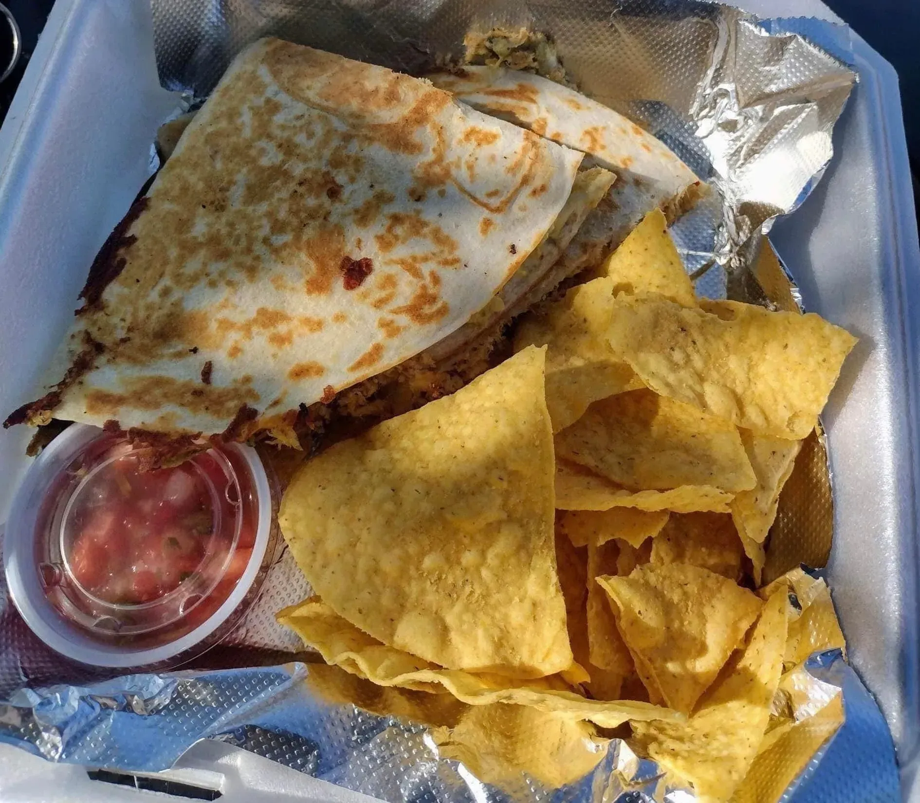 Takeout container with quesadilla wedges, tortilla chips, and a small cup of salsa