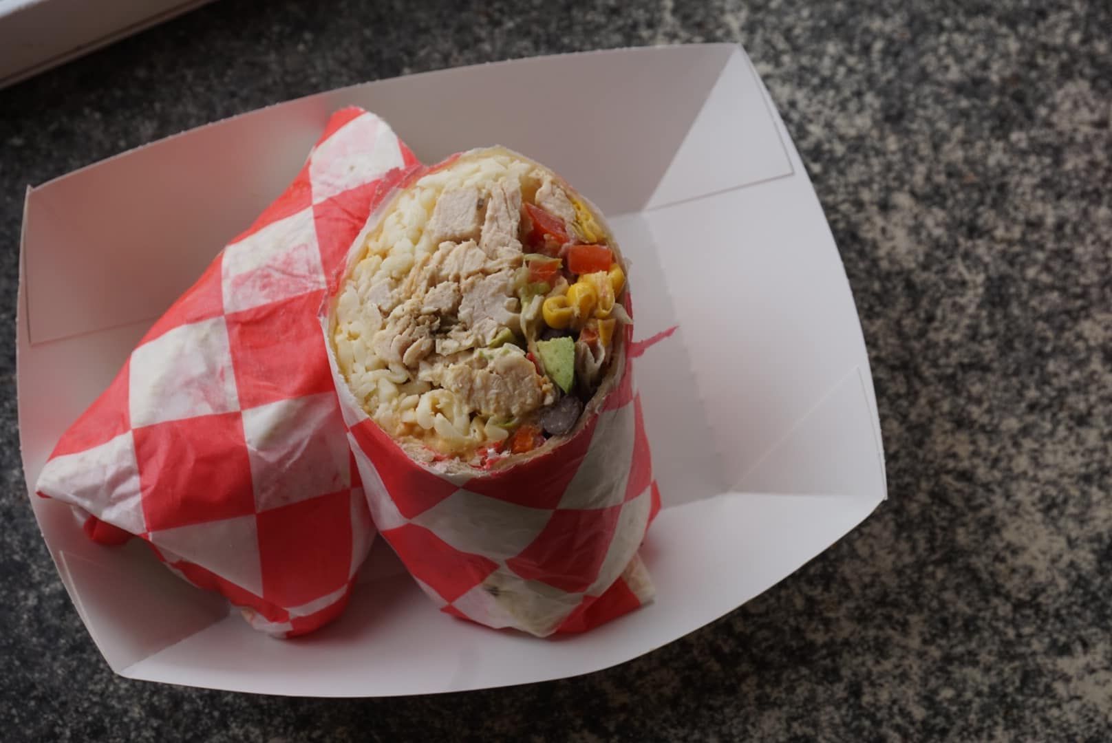Wrapped sandwich on a tray, with one end open showing the filling.