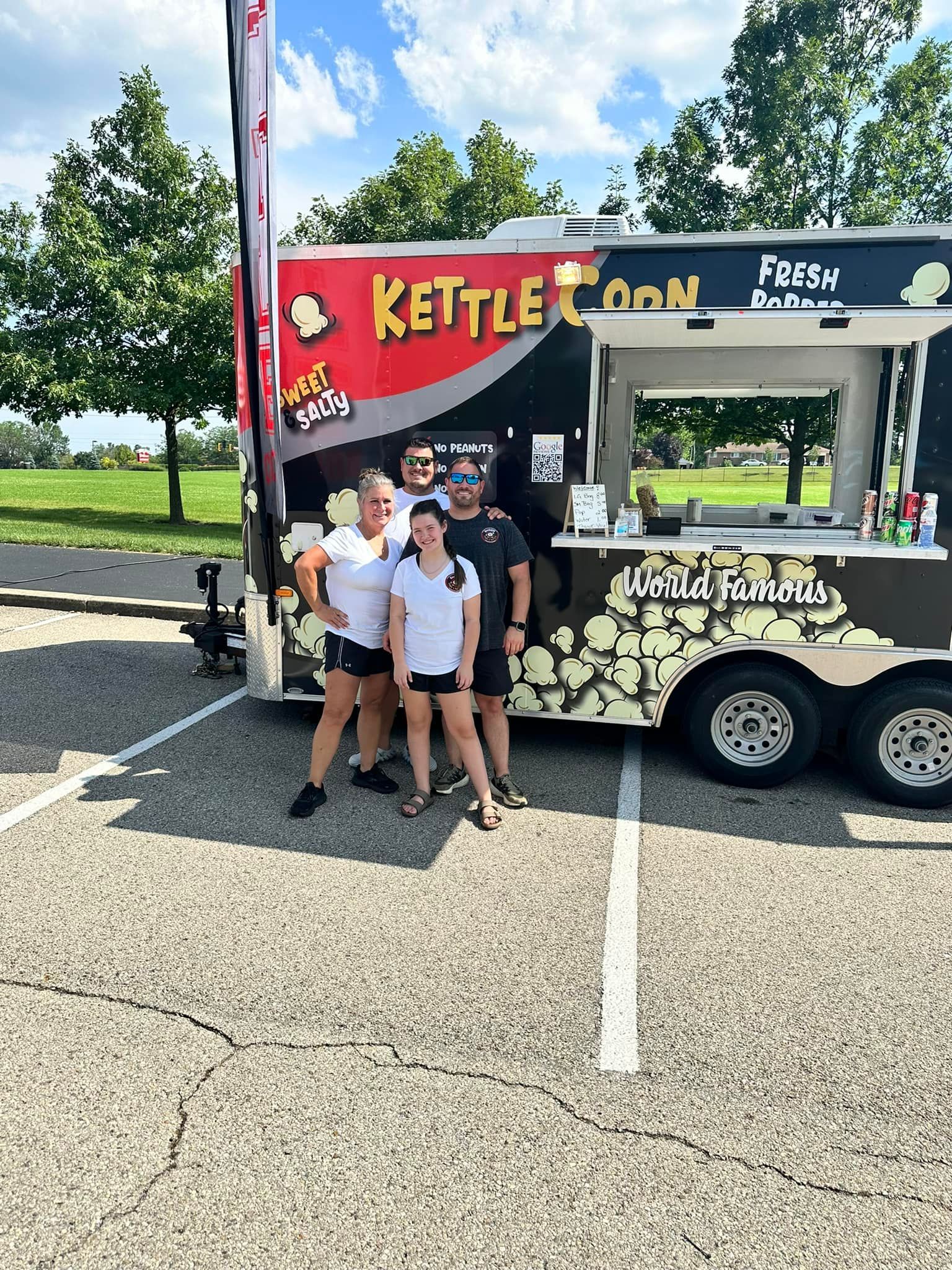 People posing by a Kettle Corn food truck on a sunny roadside.