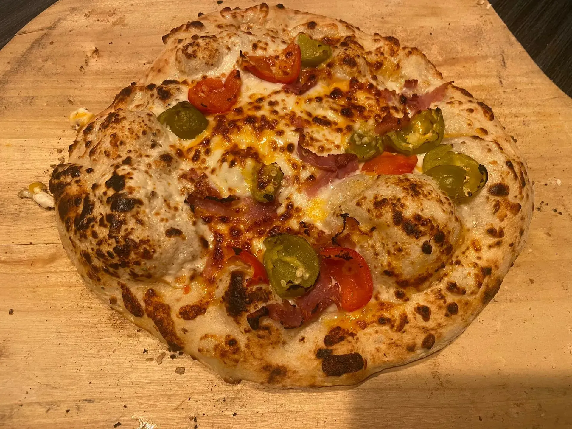 Cheesy vegetable pizza on a wooden board with green peppers and cherry tomatoes