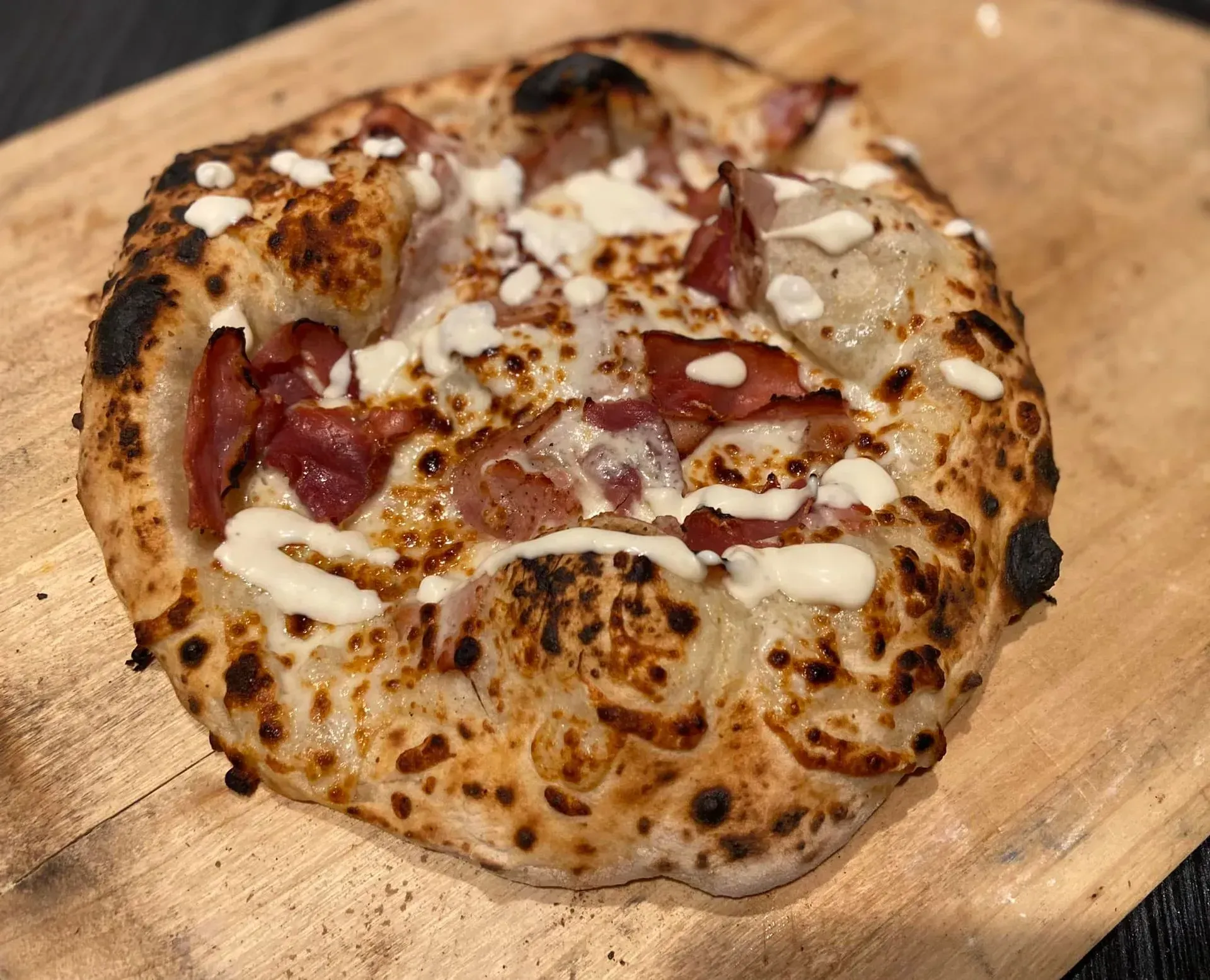 Charred flatbread pizza with melted cheese and cured meat on a wooden board