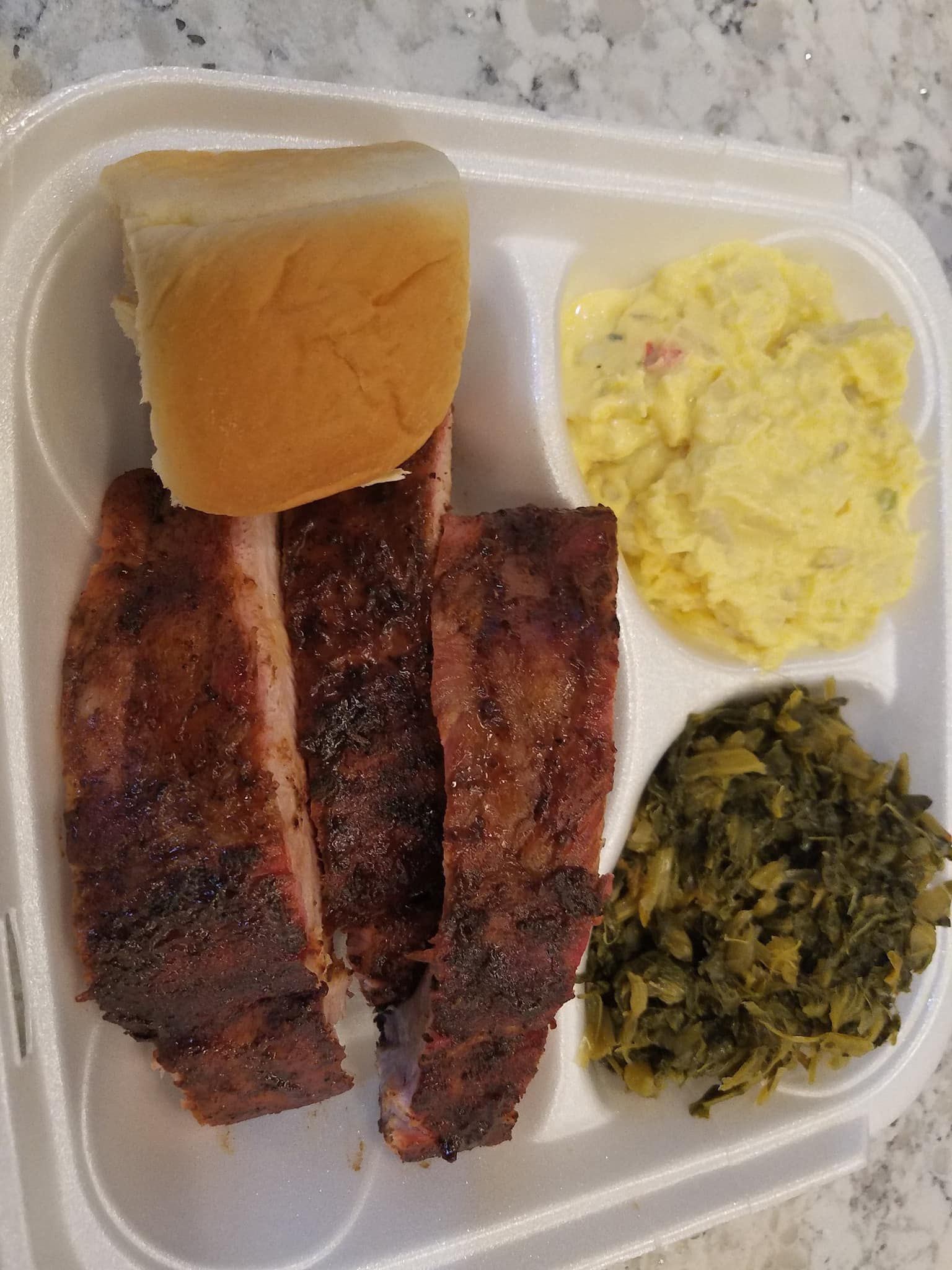 Takeout meal in a foam container: ribs, cornbread, scrambled eggs, and greens.