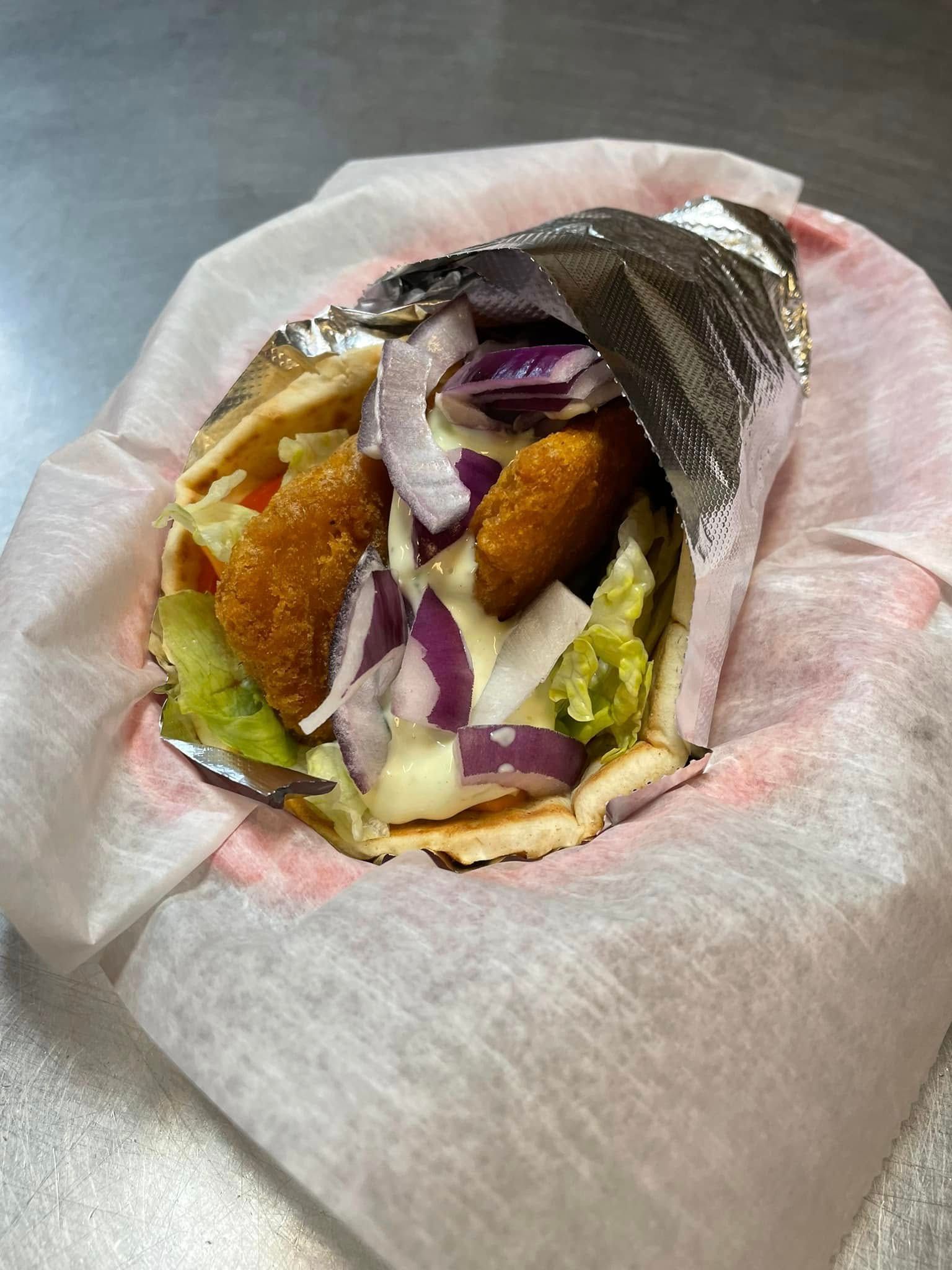 Partially eaten wrap with chicken, red onion, lettuce, and sauce in a paper wrapper on a table