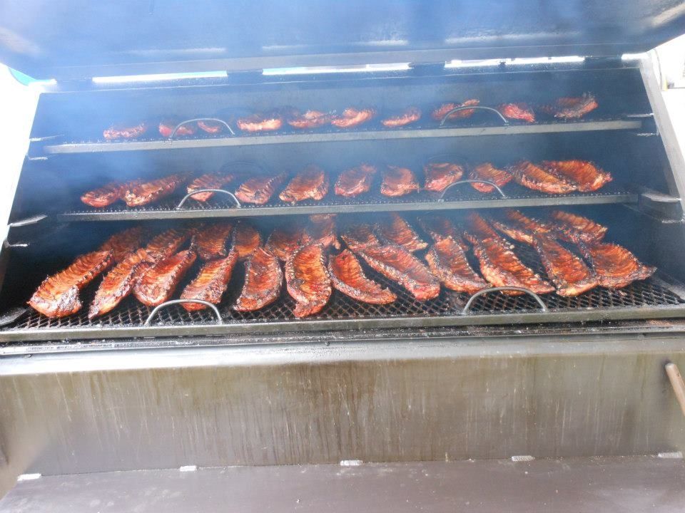 Rows of smoked fish on a grill in a stainless-steel smoker, with smoke rising.