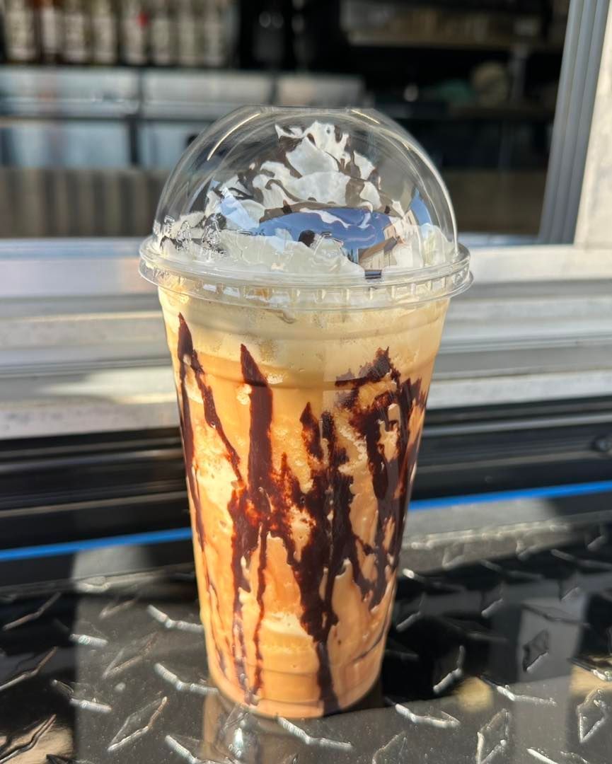 Iced caramel frappuccino in a clear cup with chocolate drizzle and whipped cream, on a counter.