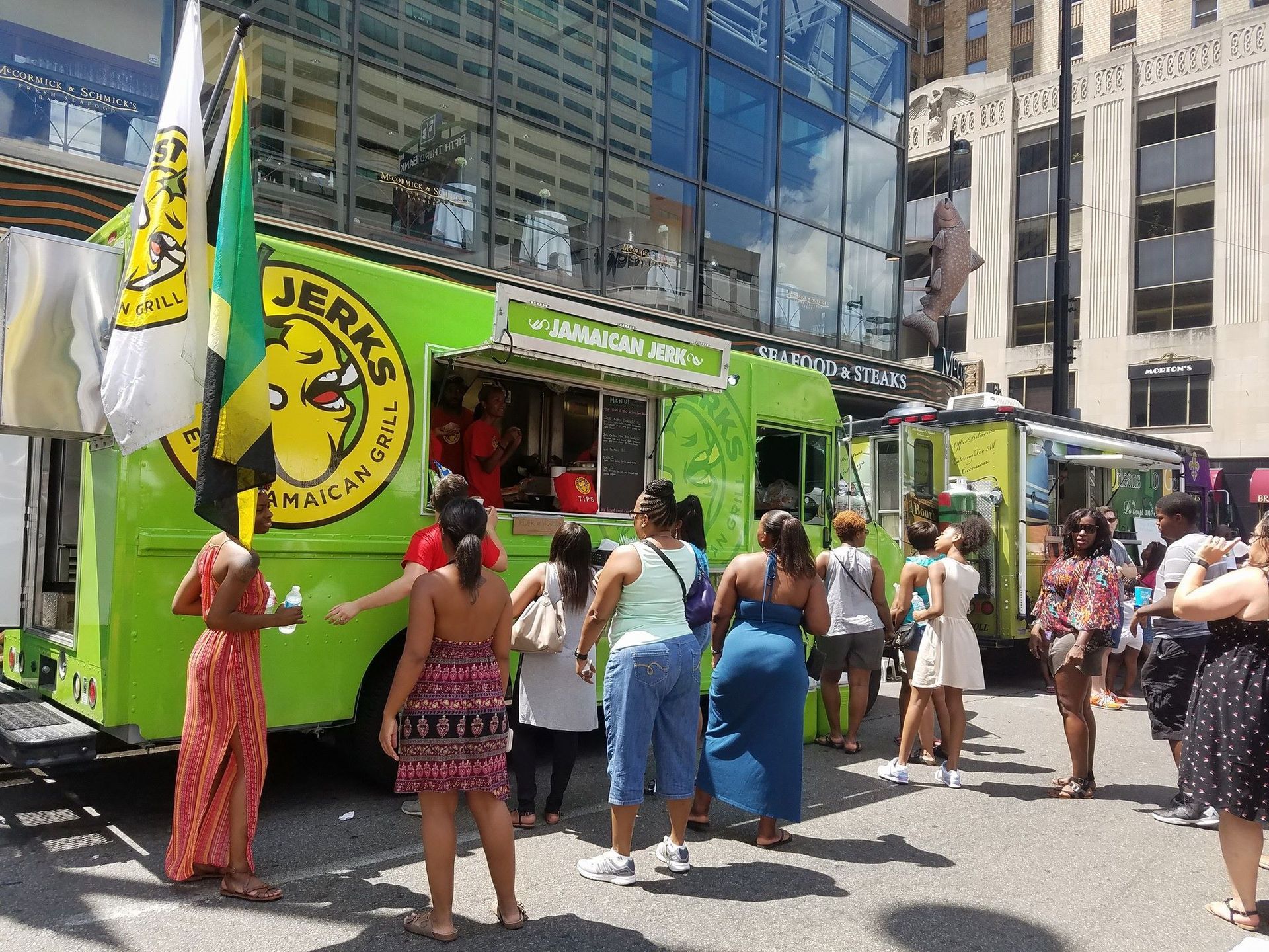 Green food truck serving people on a busy city street under tall buildings