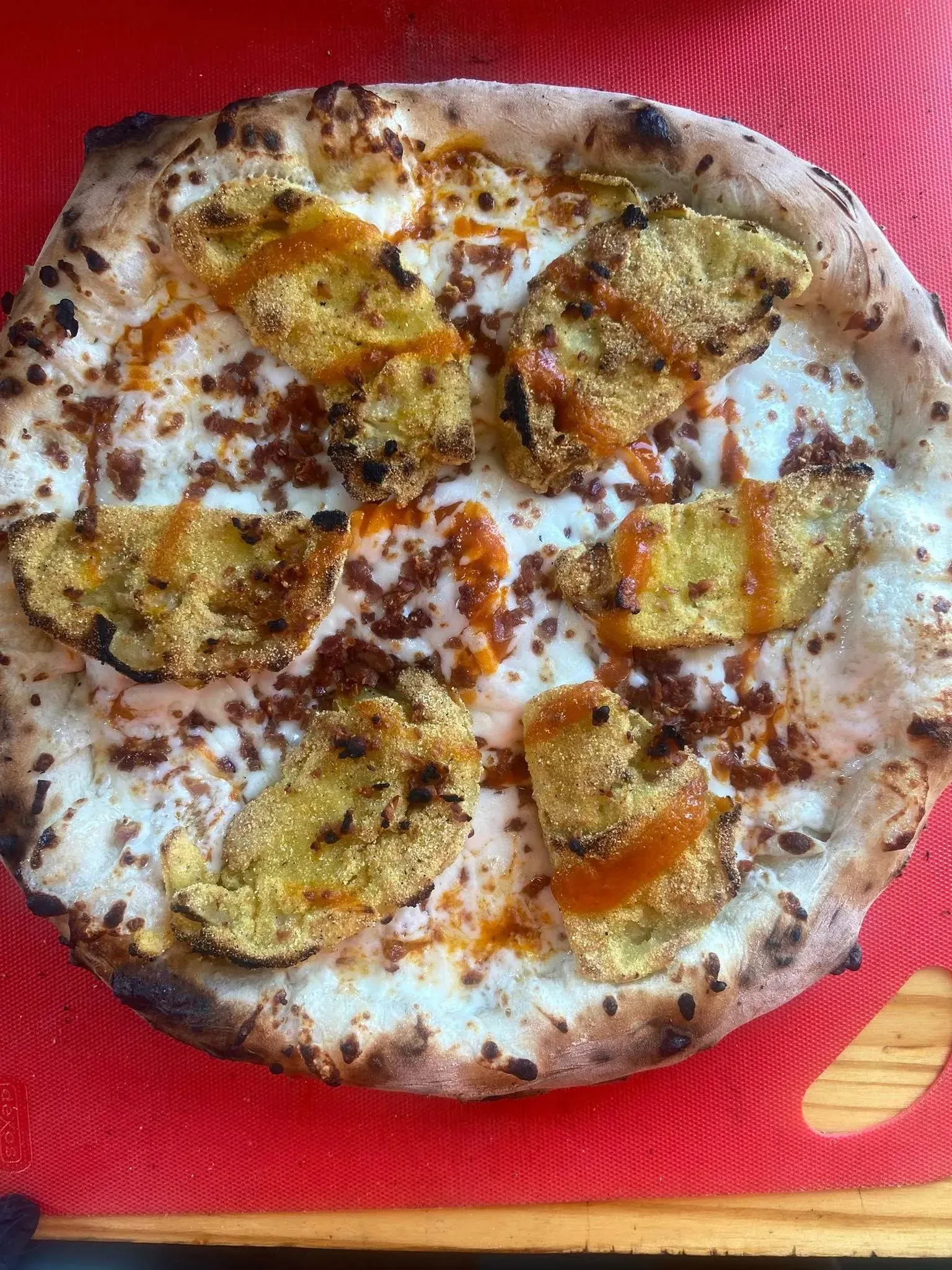 Round pizza with white cheese and golden toppings on a red textured placemat.