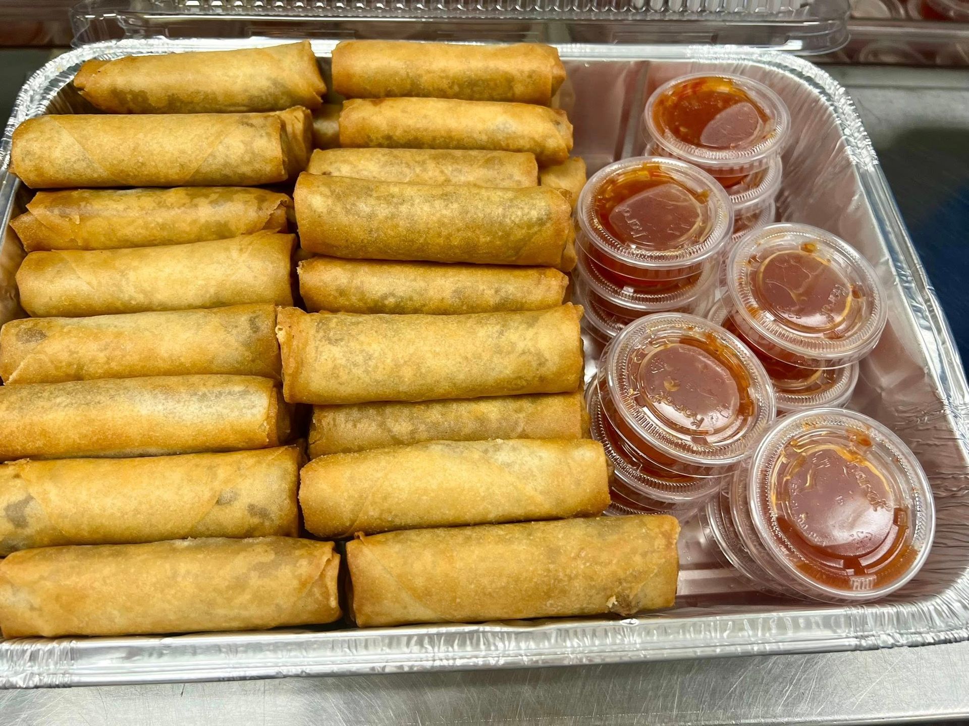 Tray of golden fried spring rolls with small cups of dipping sauce on the side