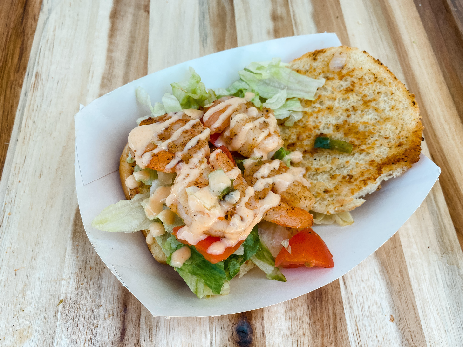 Open sandwich with lettuce, tomato, and sauce in a paper tray on a wooden table