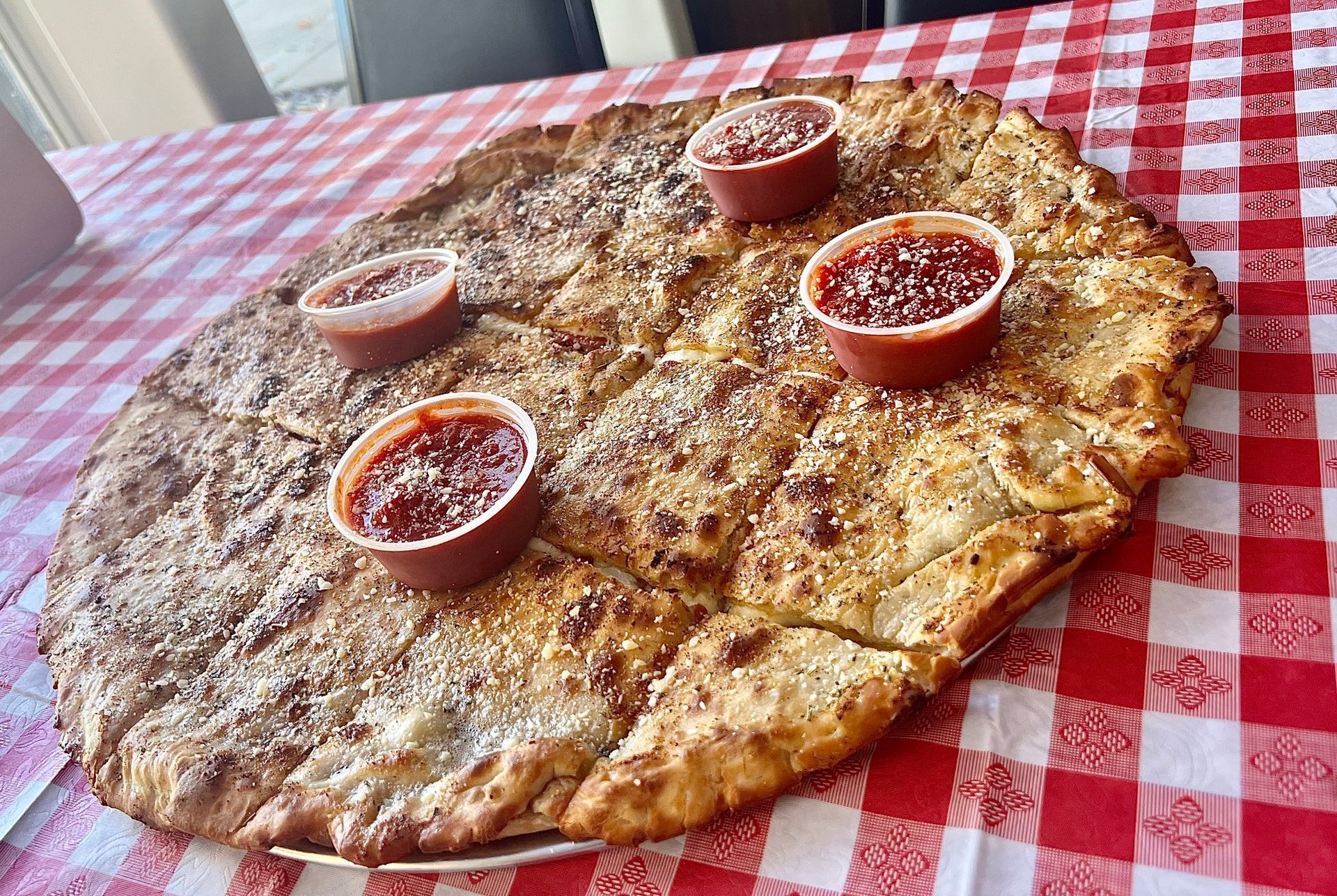 Large flatbread with dipping sauces on a red-and-white checkered tablecloth