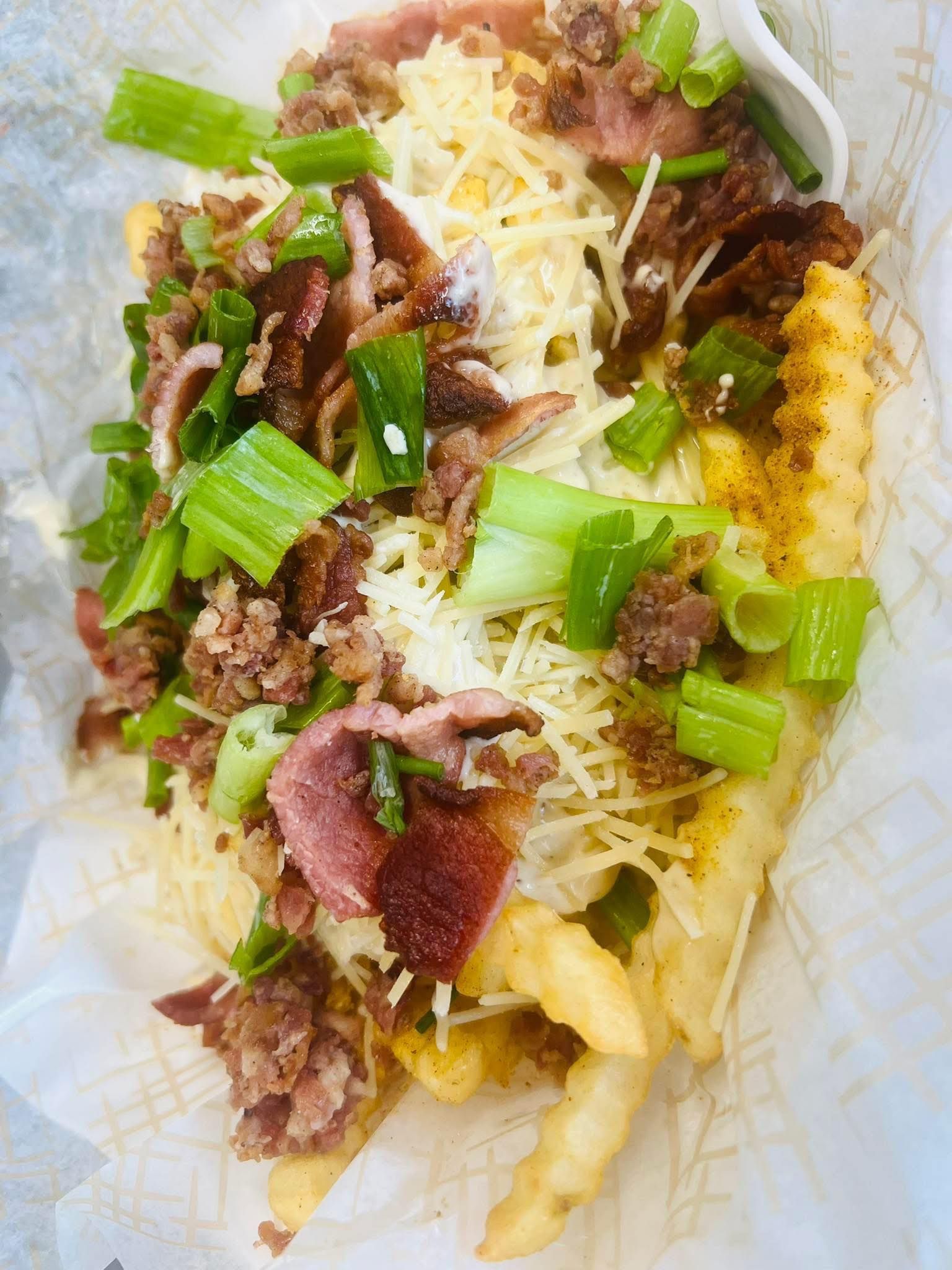 Loaded waffle fries topped with chopped beef, melted cheese, and green onions on white paper.