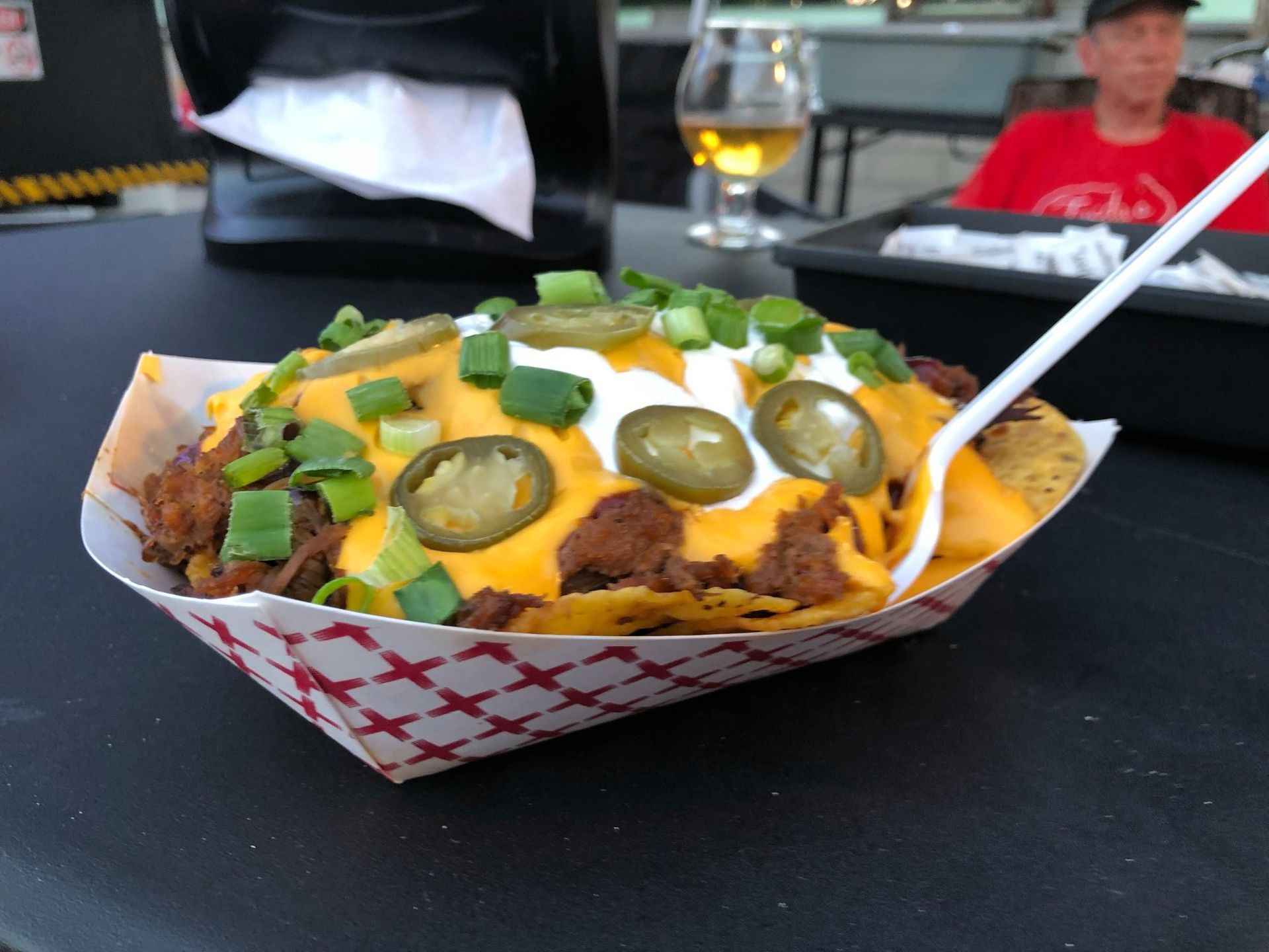 Tray of loaded nachos with cheese, jalapeños, and sour cream on a table outdoors