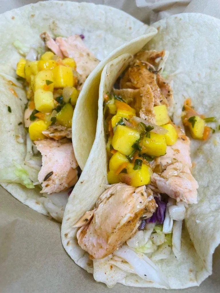 Two fish tacos topped with mango salsa on soft tortillas