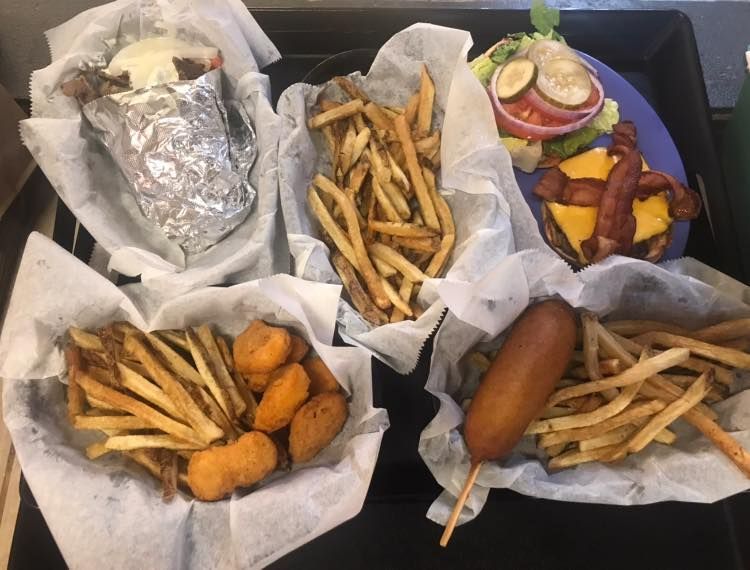 Assorted fast food with fries, a hot dog, burger, and fried snacks arranged in trays on a black table