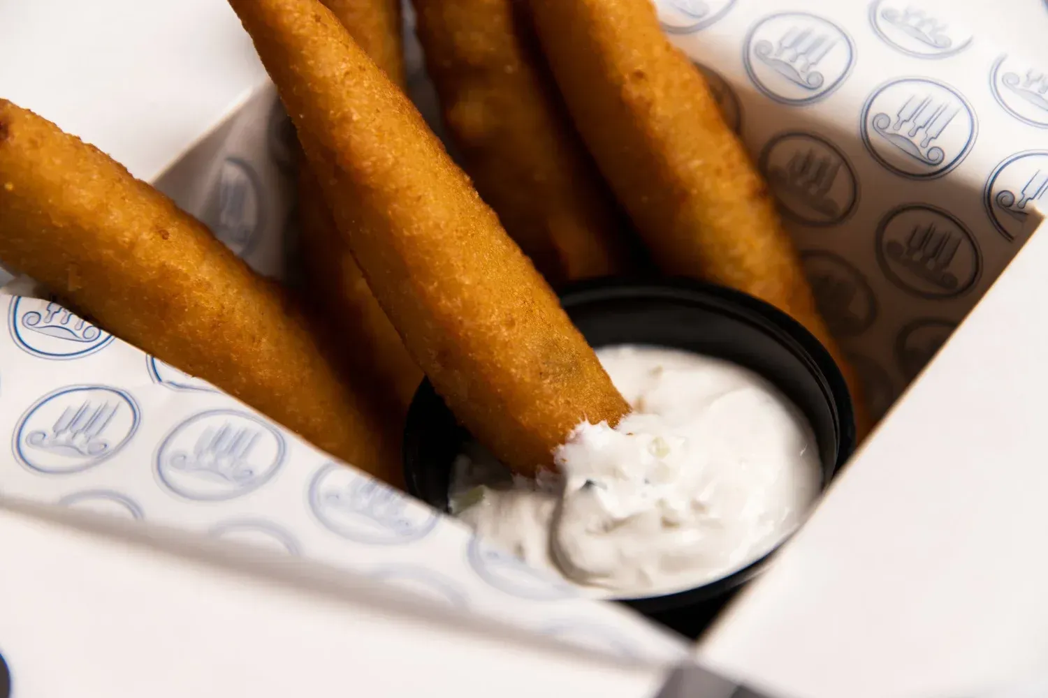 Breaded fried sticks with a white dipping sauce in a paper-lined tray.