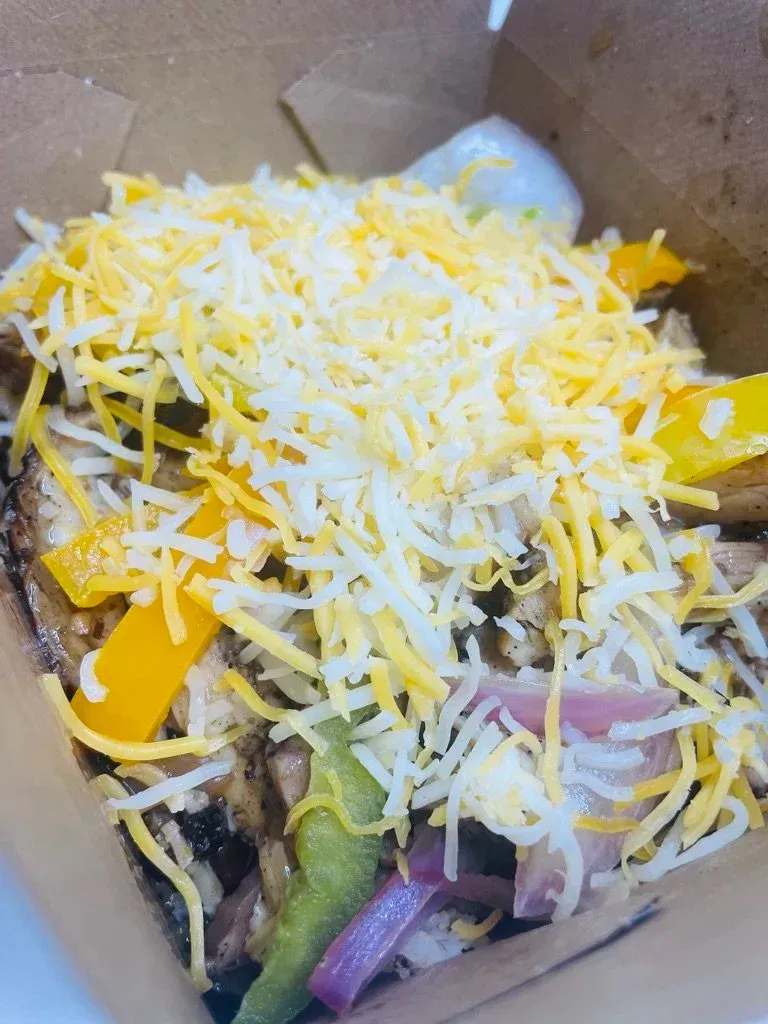 Takeout salad in a brown bowl with shredded cheese, greens, and sliced vegetables