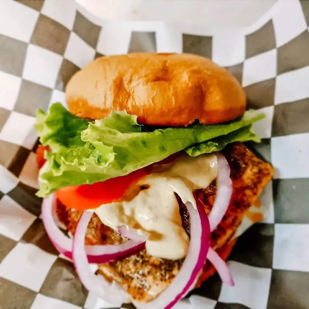 Close-up of a burger with lettuce, tomato, onion, and melted cheese on checkered paper