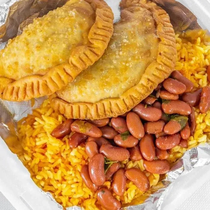 Two fried empanadas over yellow rice and beans wrapped in foil
