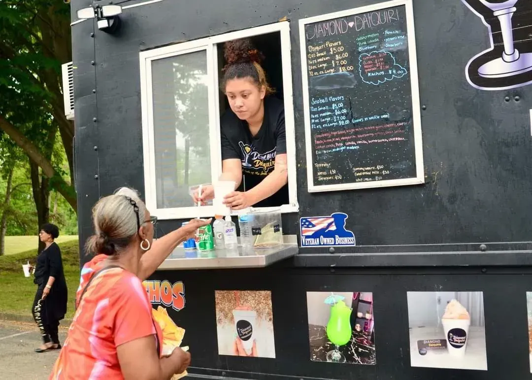 Woman ordering at a food truck through service window, with menu board and drink images displayed.