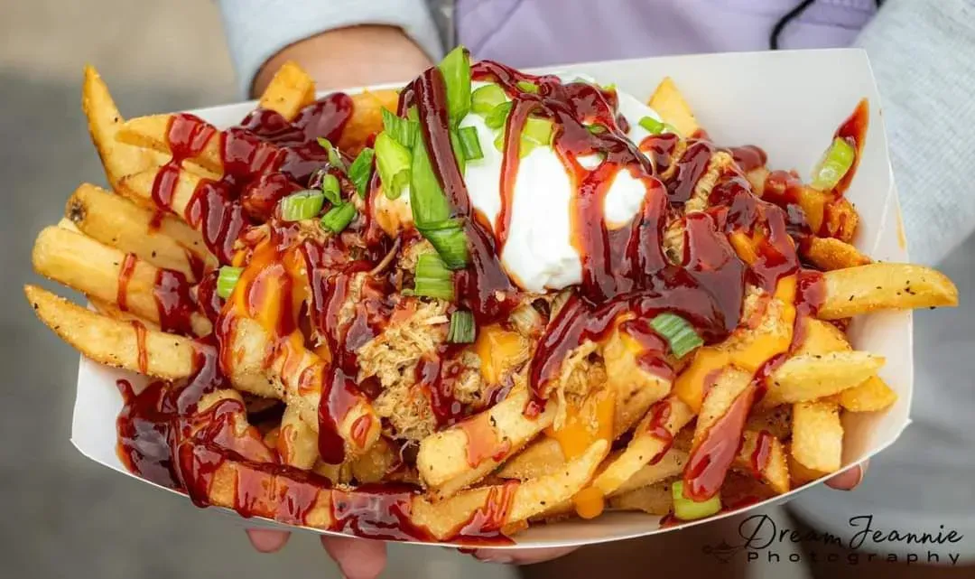 Loaded fries topped with cheese sauce, bacon bits, green onions, sour cream, and drizzled sauce on a plate