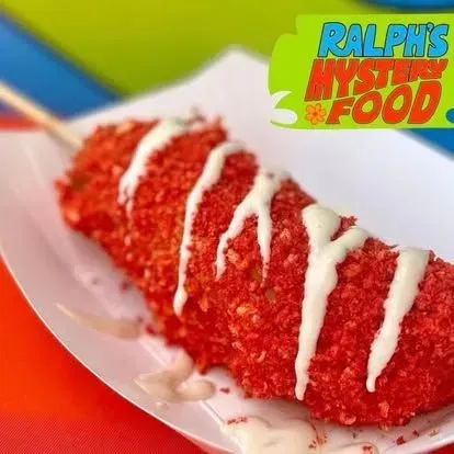 Red snack on a plate, coated in crumbs and drizzled with white sauce.