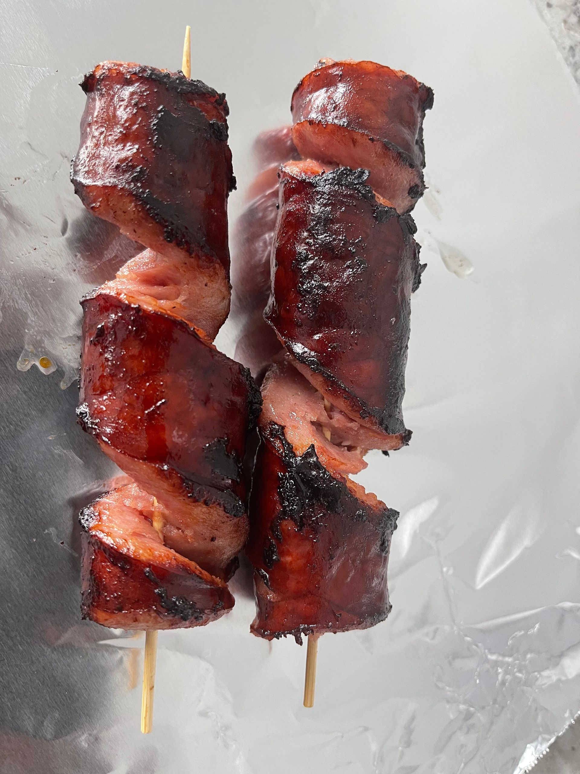 Two skewers of glazed bacon-wrapped meat on a white plate