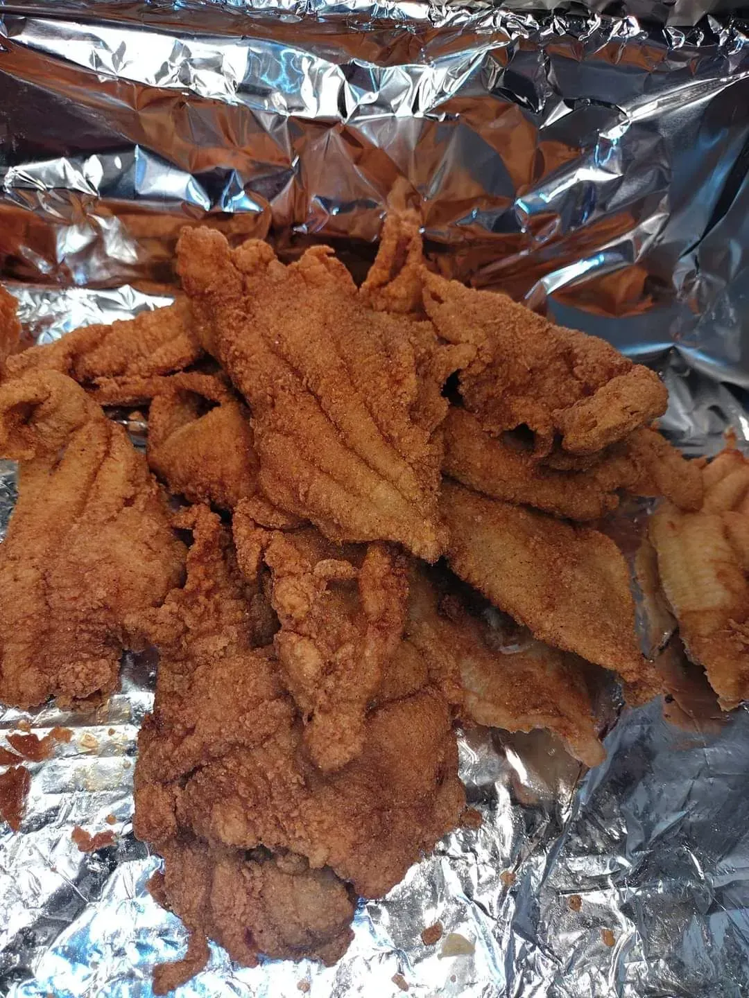 Pile of breaded fried strips on crinkled aluminum foil