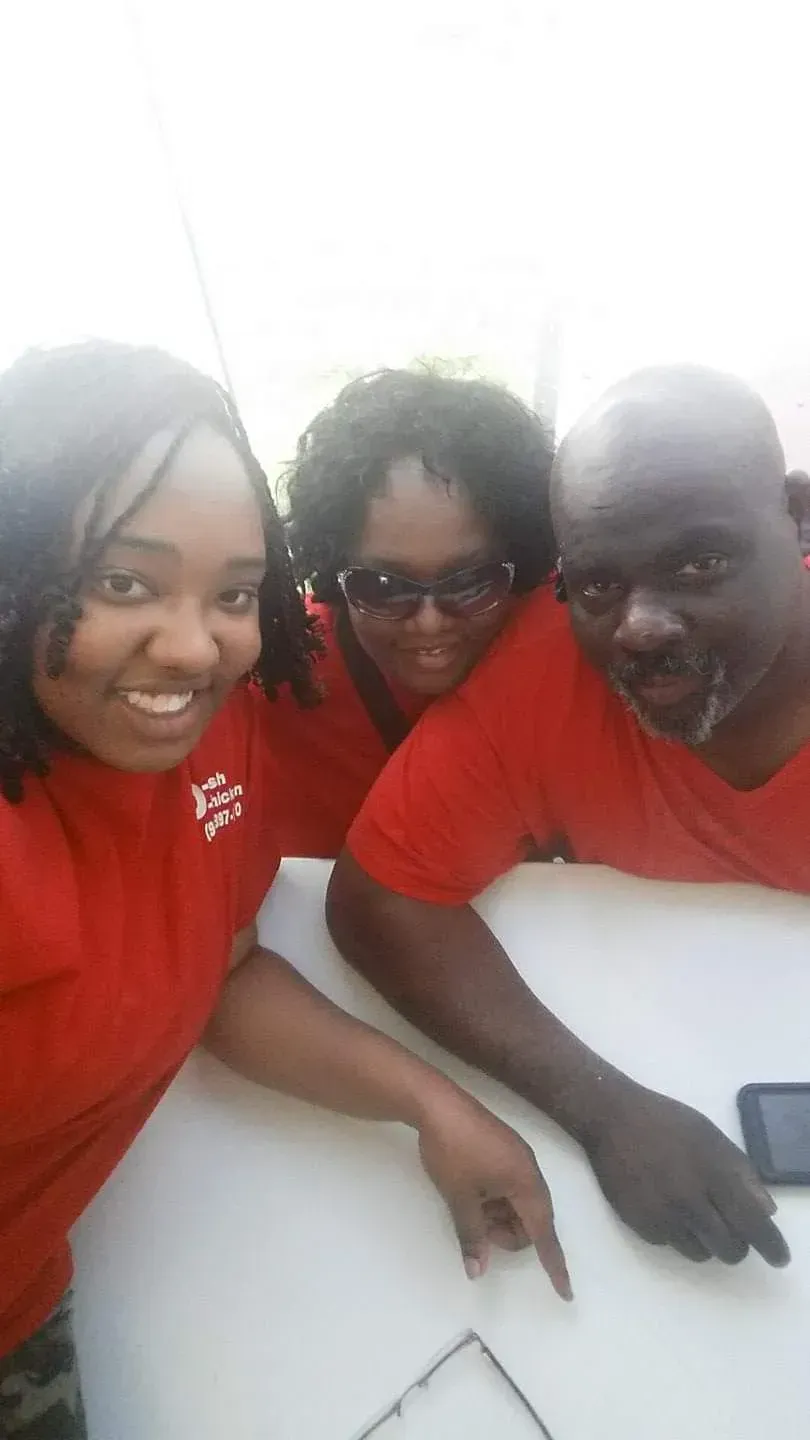 Three people in red shirts smile and point at a smartphone on a white table.