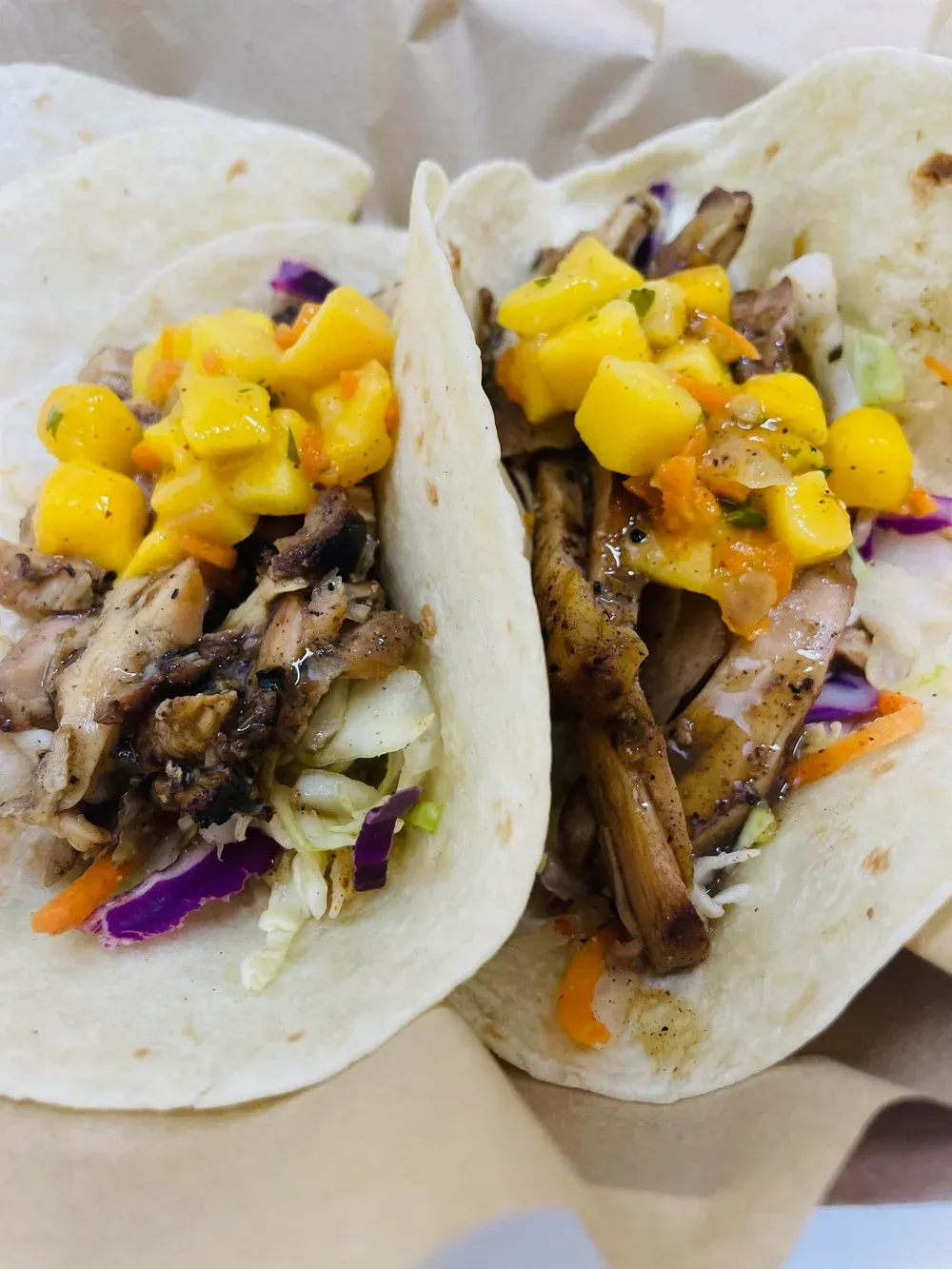 Two tacos with shredded meat, purple cabbage, and mango salsa on a plate